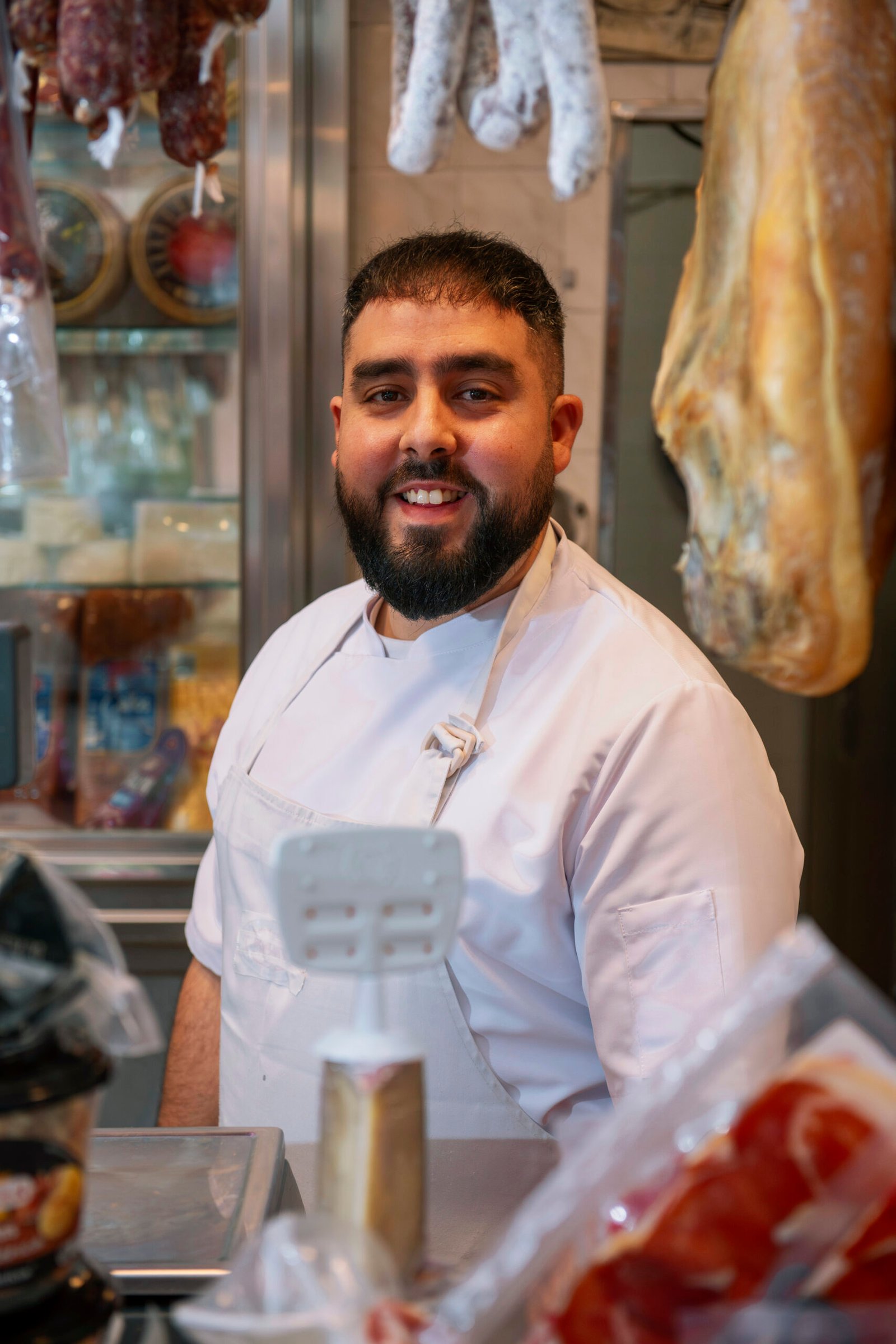Smiling butcher working diligently in a shop, skillfully slicing exquisite iberian ham while engaging with customers at the counter